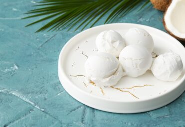 Plate with tasty coconut ice cream on color background